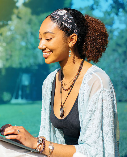 A female student is smiling as she looks down to her laptop, as she has her hands hovering slightly over its keyboard.