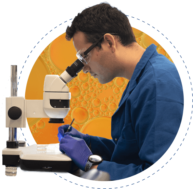 A man in laboratory attire is looking into the lens of a microscope. 